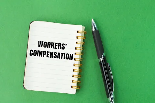 Words “WORKERS’ COMPENSATION” in a notebook next to a pen.