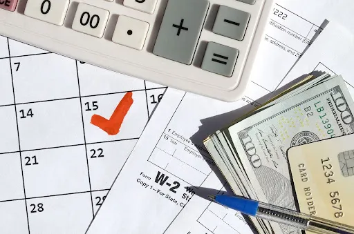 W-2 form next to a calculator, money, a credit card, pen, and calendar.