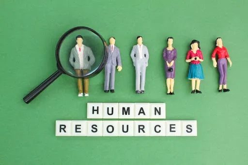 Models of people with a magnifying glass and the words “HUMAN RESOURCES” on word tiles.