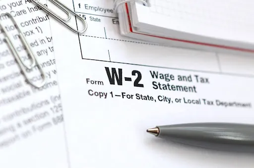 Close-up view of a w-2 form next to a notebook, paperclips, and a pen.