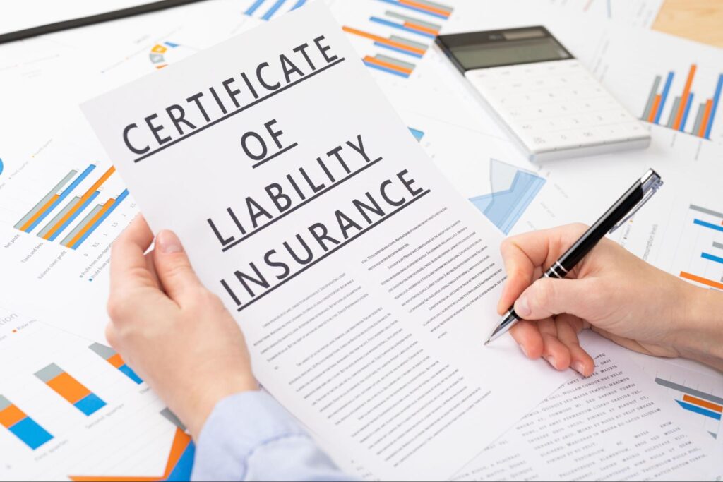 Close-up of an executive signing a liability insurance certificate near data charts and a calculator.
