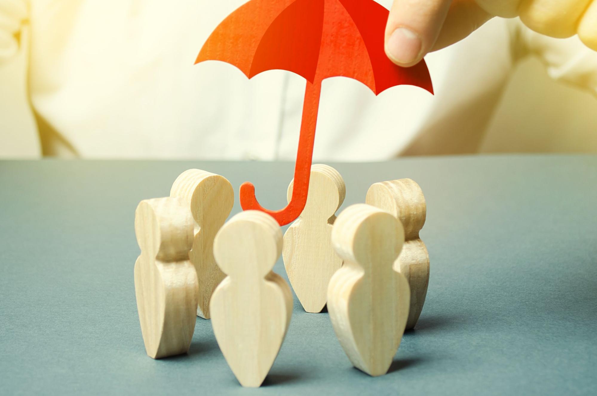 A red mini umbrella covering wooden figures, symbolizing protection under the employer’s liability insurance.