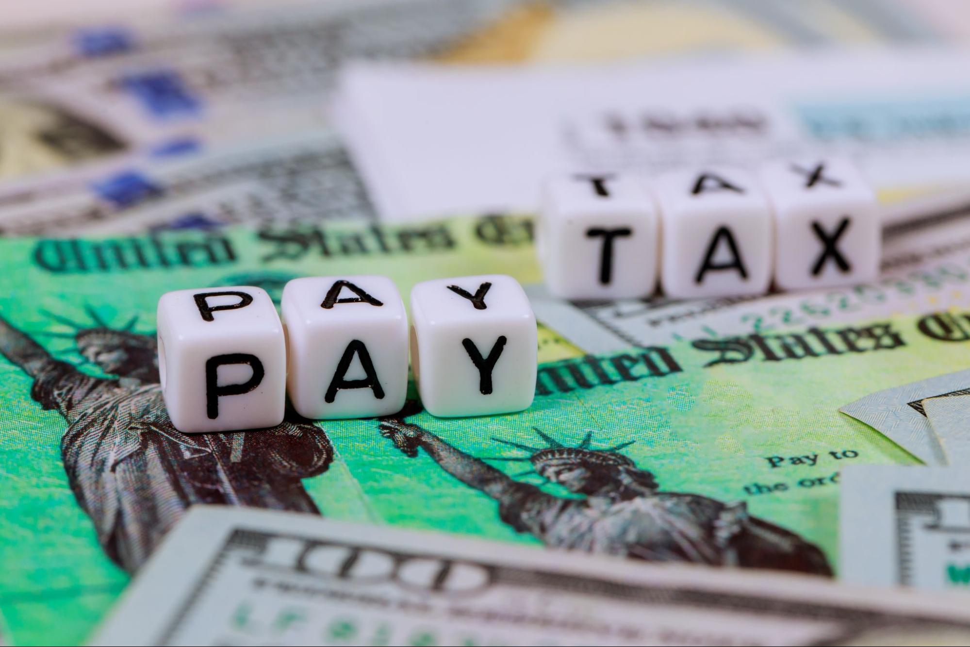 Lettered cubes spelling out "PAY" and "TAX" on top of banknotes and tax forms.