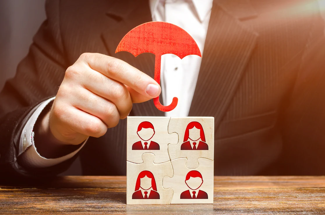 A man holds an umbrella over images of his employees to symbolize insurance.