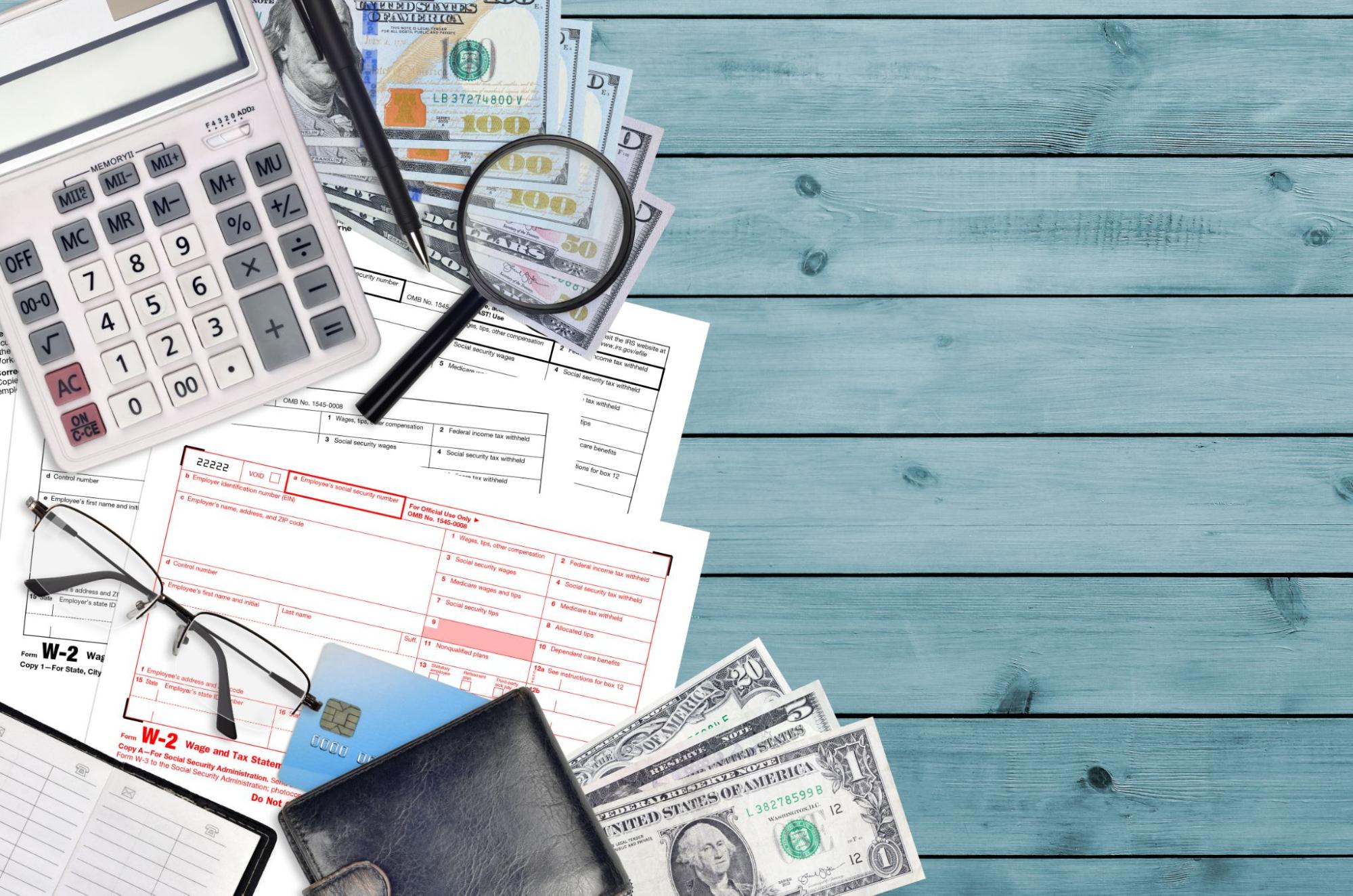 IRS Form W-2 Wage and Tax Statement on a table with a calculator, pen, eyeglasses, a black wallet, and a magnifying glass