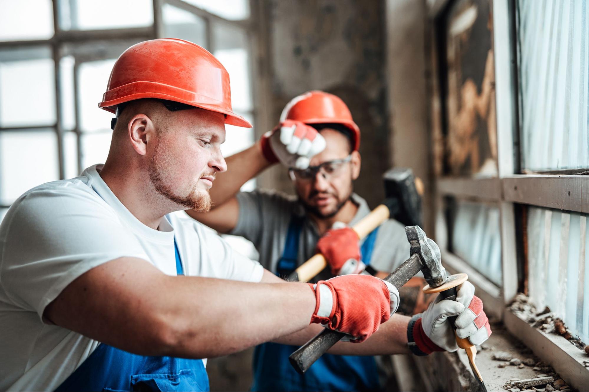 Two builders removing old plaster from an exposed brick wall